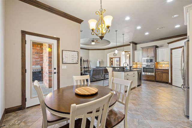 dining space featuring ceiling fan with notable chandelier, crown molding, and sink