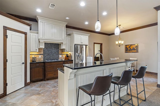 kitchen with a breakfast bar, stainless steel appliances, a kitchen island with sink, pendant lighting, and white cabinets