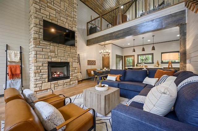 living room with a stone fireplace, light hardwood / wood-style flooring, a towering ceiling, and a notable chandelier