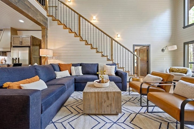 living room featuring a high ceiling, light wood-type flooring, plenty of natural light, and wood walls