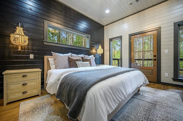 bedroom featuring dark hardwood / wood-style floors, access to outside, wooden walls, and a chandelier