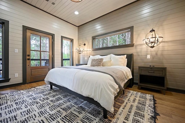 bedroom featuring hardwood / wood-style flooring, a notable chandelier, and wood walls