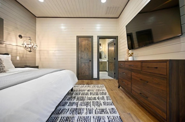 bedroom featuring a chandelier, light hardwood / wood-style flooring, ensuite bath, and wooden walls