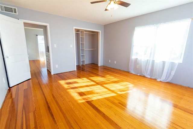 unfurnished bedroom featuring a closet, hardwood / wood-style flooring, a spacious closet, and ceiling fan