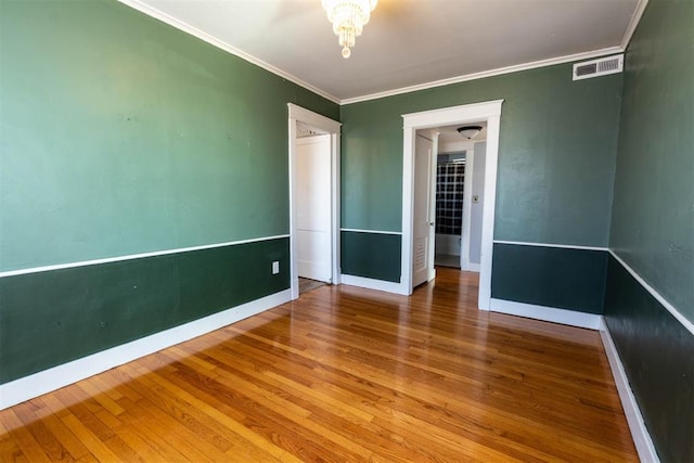 spare room featuring hardwood / wood-style floors, an inviting chandelier, and ornamental molding