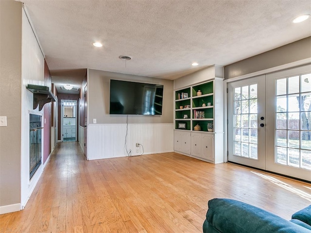 living room with french doors, a textured ceiling, and light wood-type flooring