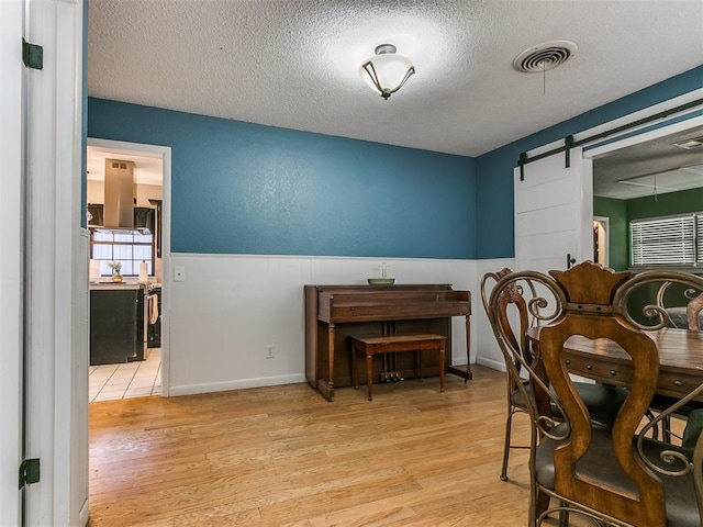 dining room featuring a barn door, light wood-type flooring, and a textured ceiling