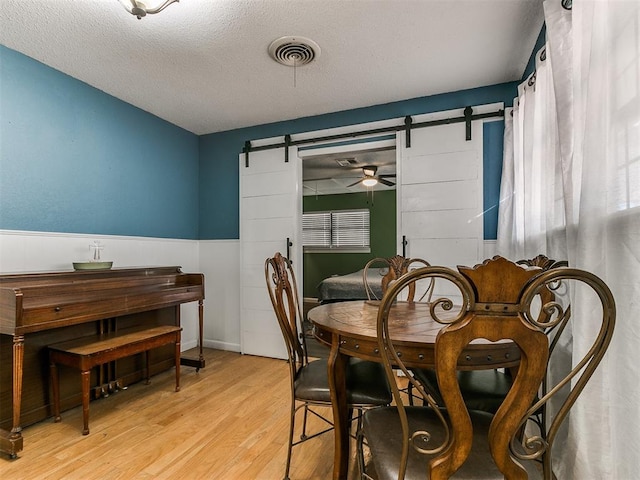 dining space featuring a barn door, ceiling fan, light hardwood / wood-style flooring, and a textured ceiling