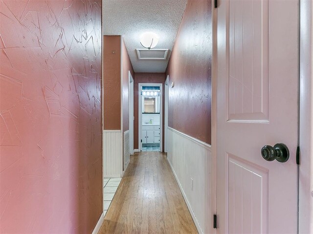 hallway with light hardwood / wood-style flooring, a textured ceiling, and sink