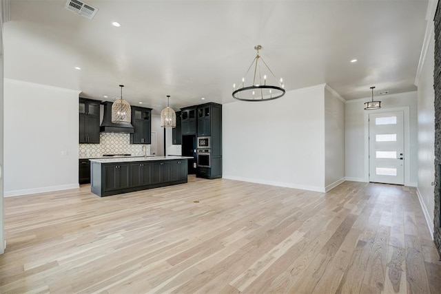 kitchen featuring decorative light fixtures, light hardwood / wood-style floors, custom exhaust hood, and an island with sink