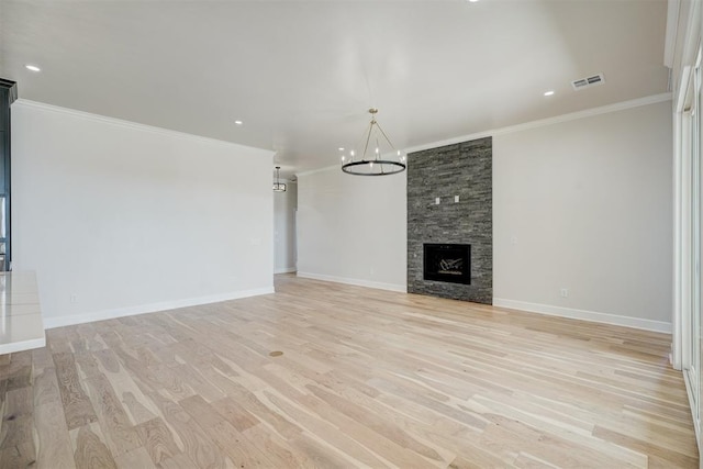 unfurnished living room featuring a notable chandelier, crown molding, a fireplace, and light hardwood / wood-style flooring