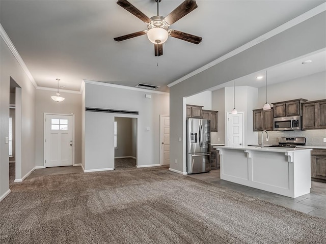 kitchen featuring appliances with stainless steel finishes, ornamental molding, light colored carpet, pendant lighting, and an island with sink