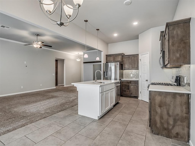 kitchen with stainless steel appliances, light colored carpet, white cabinets, hanging light fixtures, and an island with sink