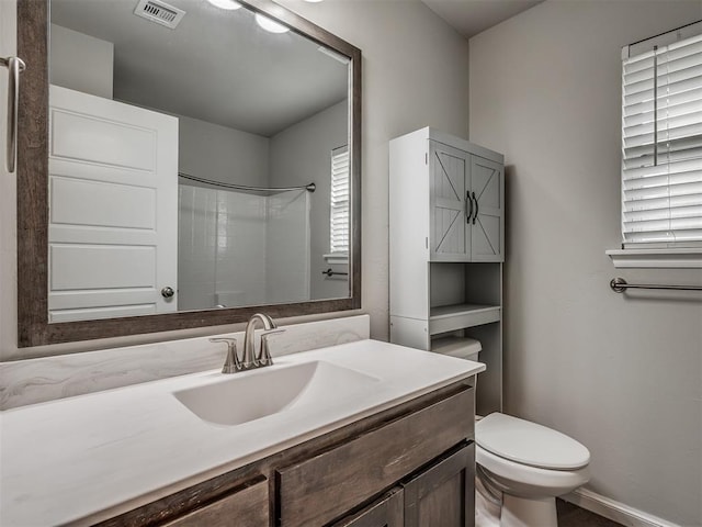 bathroom with toilet, vanity, a healthy amount of sunlight, and walk in shower