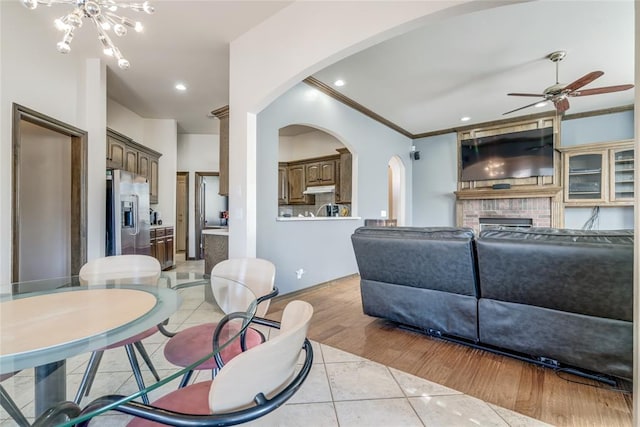 living room featuring ceiling fan with notable chandelier, light tile patterned flooring, crown molding, and a fireplace