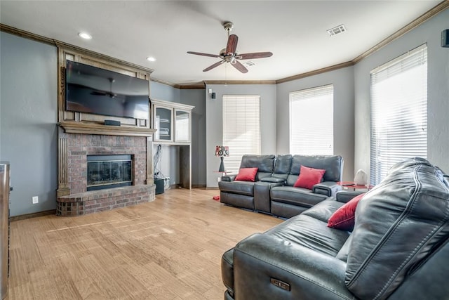 living room featuring ceiling fan, light hardwood / wood-style floors, ornamental molding, and a fireplace