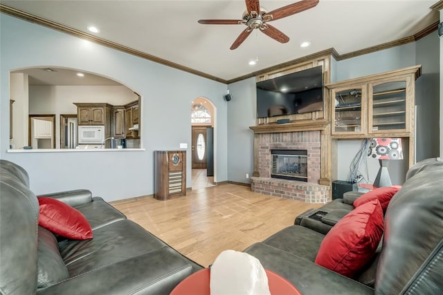 living room with ceiling fan, crown molding, light hardwood / wood-style floors, and a brick fireplace