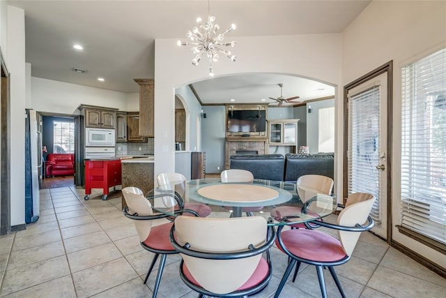 dining space with light tile patterned floors, ceiling fan with notable chandelier, a wealth of natural light, and ornamental molding