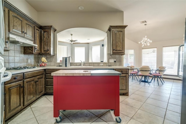 kitchen featuring ceiling fan with notable chandelier, a kitchen island, stainless steel gas cooktop, and light tile patterned flooring