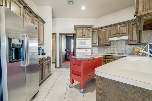 kitchen featuring sink, a kitchen island, tasteful backsplash, white appliances, and light tile patterned floors