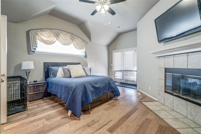 bedroom featuring a tile fireplace, ceiling fan, light hardwood / wood-style flooring, and lofted ceiling