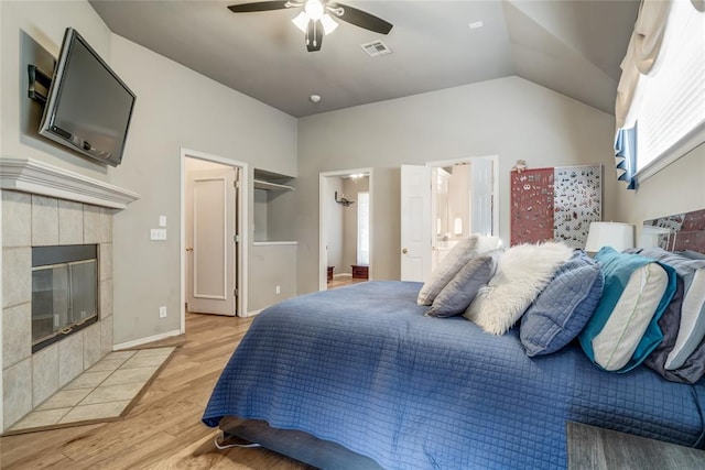 bedroom featuring lofted ceiling, a tile fireplace, ensuite bathroom, light hardwood / wood-style flooring, and ceiling fan