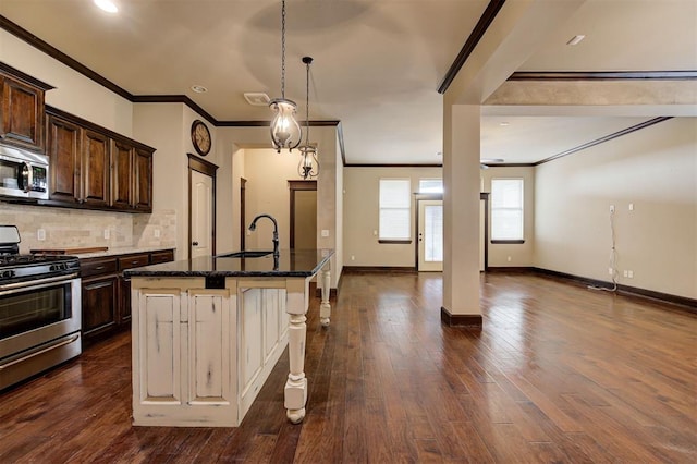 kitchen featuring dark wood-type flooring, sink, an island with sink, appliances with stainless steel finishes, and a kitchen bar