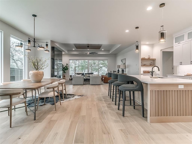 kitchen with a tray ceiling, ceiling fan, sink, pendant lighting, and white cabinets