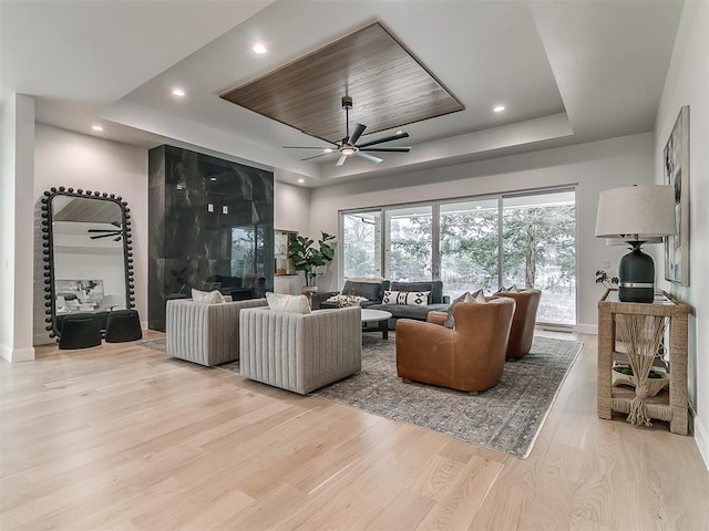 living room with ceiling fan, light hardwood / wood-style floors, and a tray ceiling