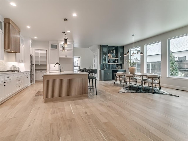 kitchen with white cabinetry, sink, an island with sink, and pendant lighting