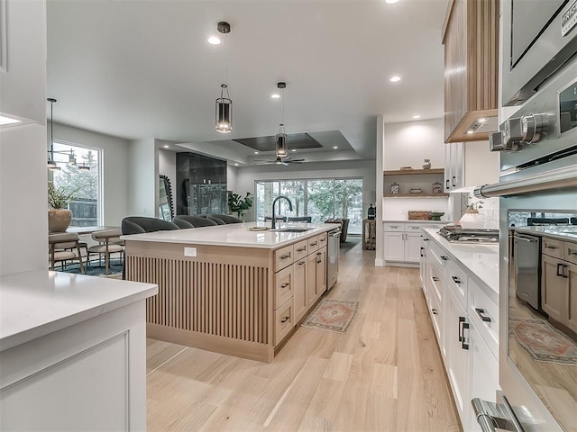 kitchen featuring a raised ceiling, a kitchen island with sink, sink, and hanging light fixtures