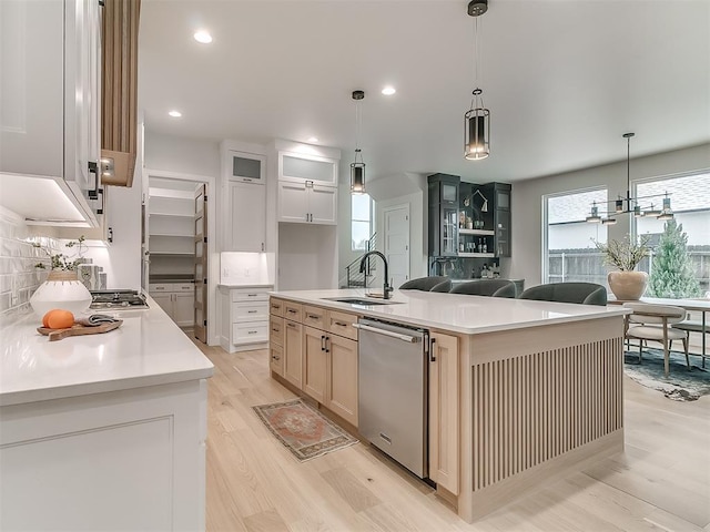 kitchen featuring sink, decorative light fixtures, a center island with sink, dishwasher, and white cabinetry