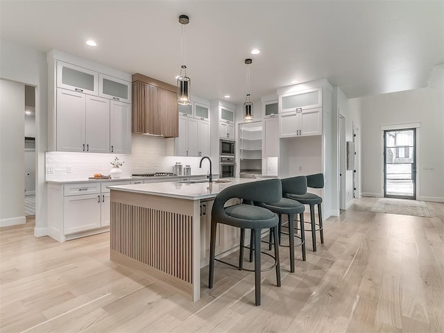 kitchen featuring white cabinetry, stainless steel appliances, an island with sink, pendant lighting, and light hardwood / wood-style floors