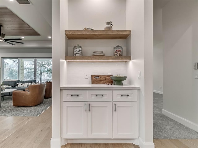 bar with ceiling fan, light hardwood / wood-style floors, and white cabinetry