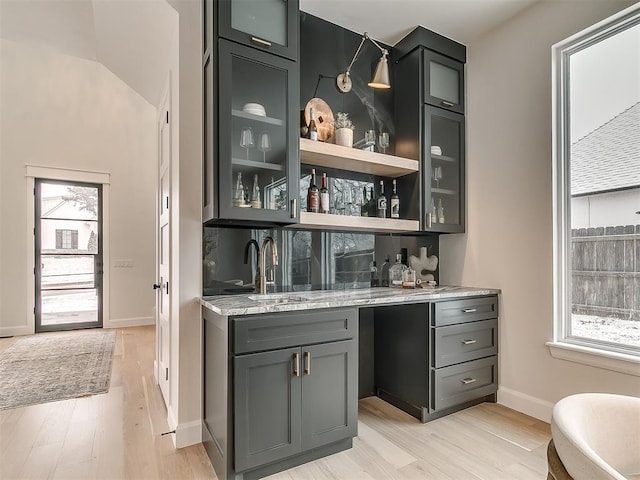 bar featuring gray cabinetry, light stone counters, light wood-type flooring, and sink