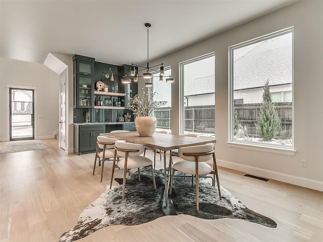 dining area with wet bar, light wood-type flooring, and an inviting chandelier