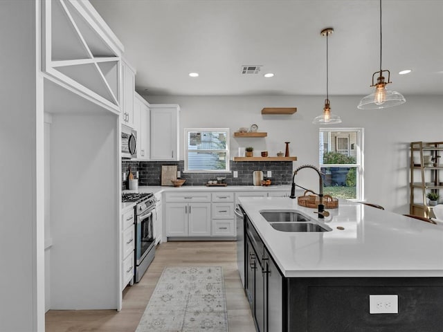 kitchen featuring pendant lighting, stainless steel appliances, a center island with sink, and sink