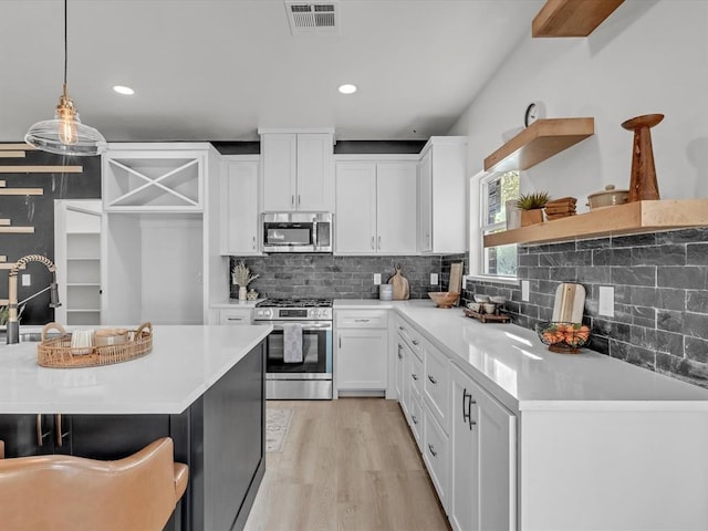 kitchen featuring pendant lighting, light wood-type flooring, appliances with stainless steel finishes, tasteful backsplash, and white cabinetry