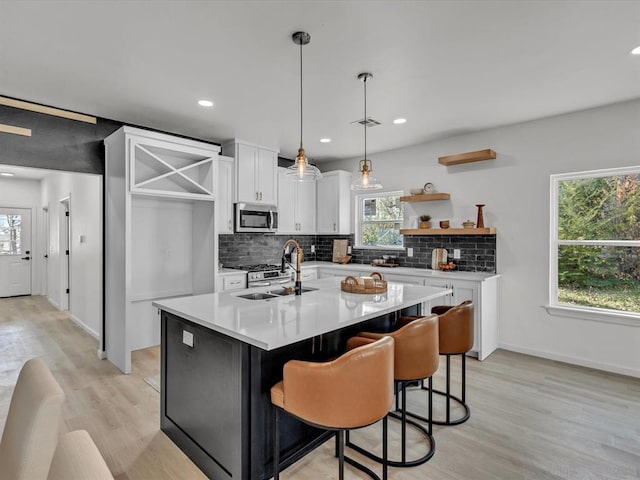 kitchen featuring sink, a breakfast bar area, hanging light fixtures, an island with sink, and white cabinets