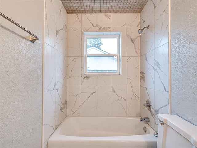 bathroom with toilet and tiled shower / bath