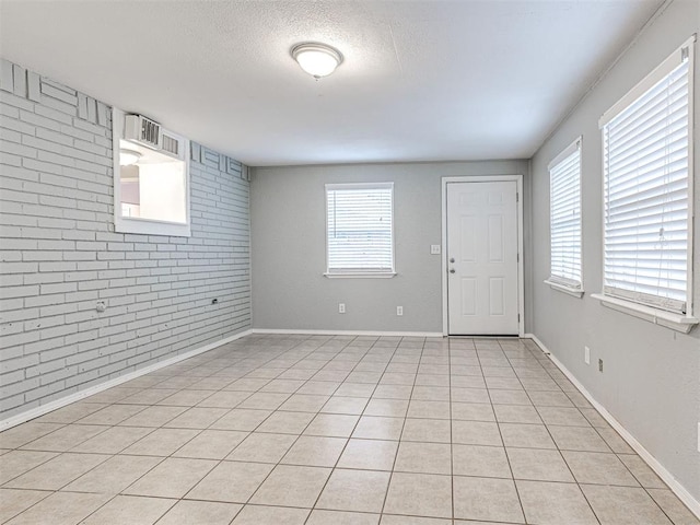 tiled empty room featuring a wealth of natural light, brick wall, and a textured ceiling