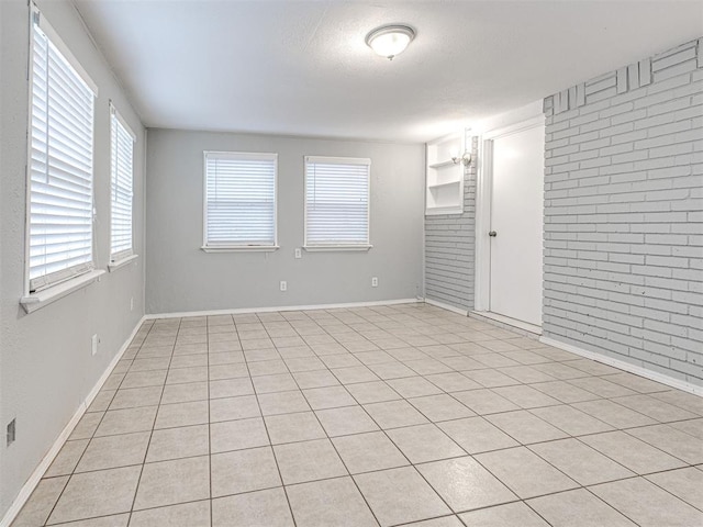 spare room featuring a chandelier, light tile patterned flooring, and brick wall