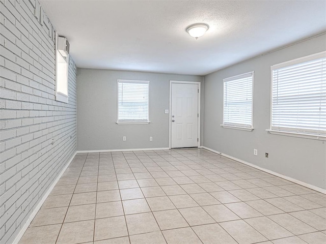 unfurnished room with light tile patterned floors, brick wall, and a textured ceiling