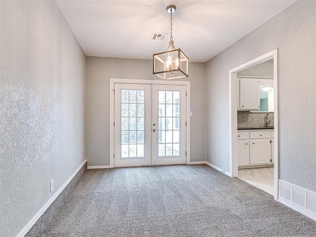 entryway featuring light carpet, french doors, and an inviting chandelier