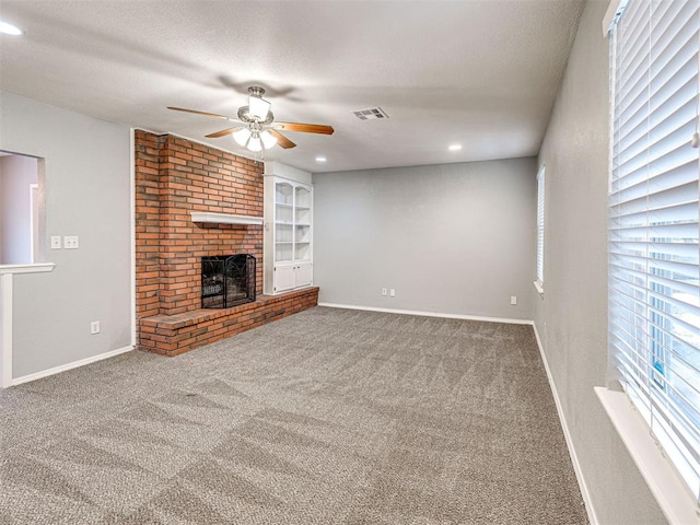 unfurnished living room with a brick fireplace, built in shelves, a textured ceiling, ceiling fan, and carpet floors