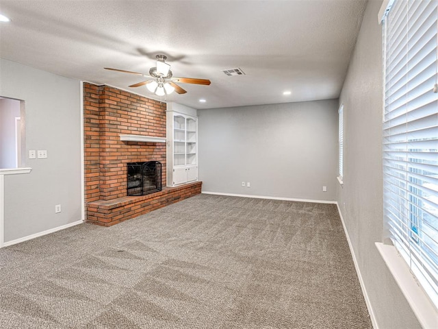 unfurnished living room featuring carpet, ceiling fan, a textured ceiling, and a brick fireplace