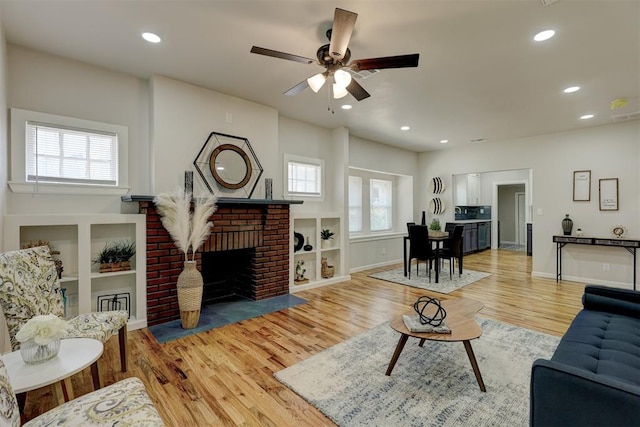 living room featuring a fireplace, light hardwood / wood-style floors, ceiling fan, and a healthy amount of sunlight