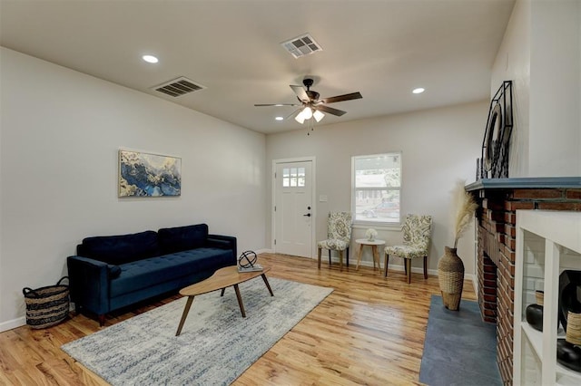 living room with ceiling fan, light wood-type flooring, and a brick fireplace