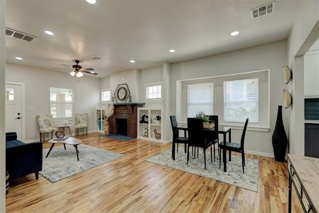 dining space with a brick fireplace, ceiling fan, plenty of natural light, and light hardwood / wood-style flooring