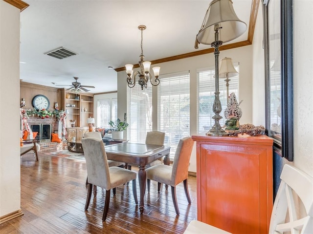 dining space with hardwood / wood-style floors, ceiling fan with notable chandelier, crown molding, and a fireplace